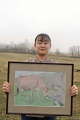 本の表紙となった作品の原画を持つ北野さん。牧場での生活の一部分を描いた
