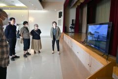 畠中さんが設計した音楽ホールの概要を紹介する動画を見る観客たち