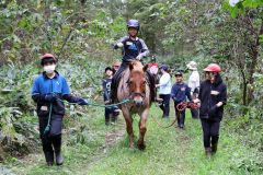 乗馬で森を歩くトレッキングを体験する児童
