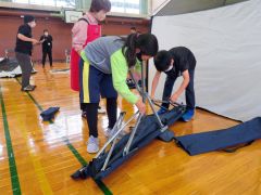 避難用の折りたたみベットの組み立てに挑戦する児童たち