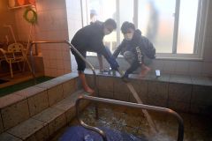 あさひ苑の浴槽にモール温泉を注ぎ込む青年部員ら（左が山崎部長）