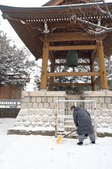 雪が降る中、「除夜の鐘」に向けて、雪かきを行う同院の池上宗恵さん。コロナ禍前につり下げていたライト（左）も今年復活し、雰囲気を盛り上げる（３１日午前９時１５分ごろ）