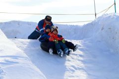 ゴムチューブで雪の滑り台を滑走し、歓声を上げる子どもたち