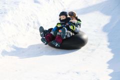 ゴムチューブで雪の滑り台を滑走し、歓声を上げる子どもたち