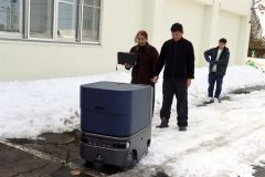 雪道を自動運転する配送ロボットと大山社長（中央）