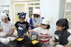講師の梅本さん（左から３人目）にアドバイスしてもらいながら玉子焼きを調理する児童ら
