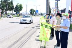 旗を振って交通安全を呼び掛けた平井会長（右）ら（ダイイチ札内店前）