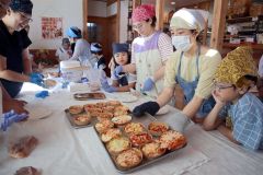 焼きあがった「ピザ風総菜パン」を運ぶ吉間さん（右から２人目）