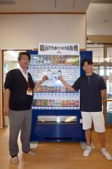 自販機に専用カードをかざす高間施設長（左）と齊藤さん（右）