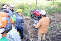 植え付け（植樹）時の位置データを活用して、苗を自動で避けて雑草を刈る下刈機を見学する参加者。