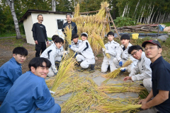 収穫した稲をはさがけする生徒たち（右が高山教諭、後方右が若山さん）