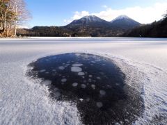 雪を払った湖面に浮かぶアイスバブルと雌阿寒岳