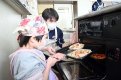 高校生に手伝ってもらいながらピザをオーブンに入れる子ども