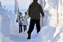 背丈以上の雪山に囲まれた歩道を歩く子ども（６日午前８時１５分ごろ、帯広市清流西１。塩原真撮影）