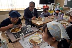 「音更高校　濃厚バターチキンカレー」をおいしそうに食べる児童らと藤森商会事業部のスーパーバイザー前谷さん（左奥から２人目）