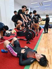 ワットバイクリレーで激走し倒れ込む梅川選手（下）とゲームを進めるスケート部員