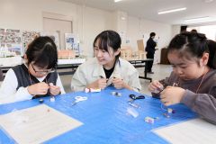 木を使ったキーホルダーを作る子どもと指導する帯広工業高生（３月３０日午前１０時５０分ごろ、帯広市児童会館。助川かおる通信員撮影）