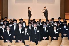 新入社員を代表して決意表明を述べる二瓶誠さん（後方右）と、関係者の前に整列する新入社員（１日午前１０時４０分ごろ、とかちプラザ。金野和彦撮影）