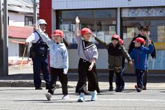 警察官らに見守られながら手を挙げて横断歩道を渡る児童（須貝拓也撮影）