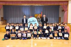 贈呈式に臨んだ関係者と贈られた絵本を手にする園児たち。後列左から山村主任、エネさん、石山所長