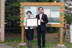 蔦井会長（左）と感謝状を贈った米沢市長。後方は今回寄贈された掲示板