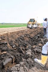 反転プラウで土を掘り起こし、河川掘削土と表土を反転させるトラクター