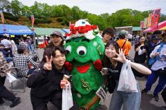 「五分咲き」のツツジをバックに、広尾サンタランドのマスコット「ツリー君」と記念写真を撮る来場者（石原秀樹通信員撮影）