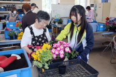 生徒（左から２人目）にアドバイスをもらって寄せ植えに挑戦する受講者（左）