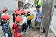 まちなかで看板を見ながら大和田学芸員（右）の説明を受ける児童（金野和彦撮影）