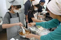 管理栄養士の梅本さん(右)にアドバイスをもらいながら弁当作りに挑戦する児童(左)