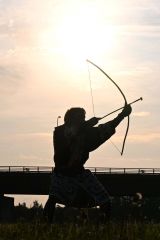 夕日を背景に弓の舞を披露する平取アイヌ保存会の男性（須貝拓也撮影）