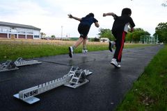 陸上競技専用ゴムマットを敷いたレーンでスパイクを履いて短距離走のトレーニングをする児童ら