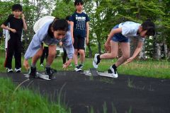 陸上競技専用ゴムマットを敷いたレーンでスパイクを履いて短距離走のトレーニングをする児童ら