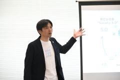 校章のオリジナルＴシャツを着けて語っている清水教頭