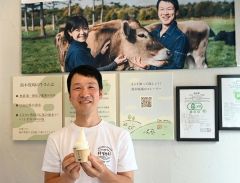 「日本初のオーガニックミルクソフトクリーム」をＰＲする鈴木さん。牧場のタペストリ―やパネルも展示している