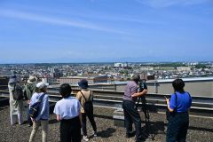 普段は立ち入ることができない帯広市役所屋上で日高山脈や市街地を眺める参加者(25日午前9時半すぎ、塩原真撮影)