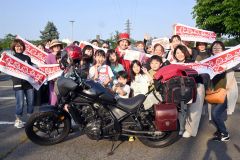 紅白の横断幕を掲げて友人らに出迎えられた日本縦断ソロツーリングを完遂した佐々木さん（中央）