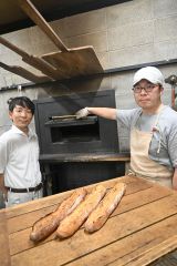 まき窯の前で新商品「バゲット風土火水」をＰＲする（右から）梅澤店長と伊藤社長