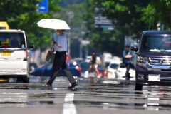 熱せられたアスファルトの上を日傘を差して歩く通行人（８日午前１１時ごろ、市内西１南１０。金野和彦撮影