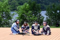 屋外で行われているアイヌの暮らしを伝える公演。本州との交易で手に入れた漆塗の行器（ほかい）のふたをたたいて歌をうたう