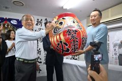 当選確実の報を受け必勝だるまに目入れする鈴木氏（左）