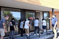 市内の「デイハウスえむず」で行われた避難訓練で、避難経路を確認後、職員に促されて冷房が効いた室内に戻る利用者ら（２４日午後２時５分）