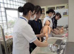 人形を使いもく浴を体験する参加者と指導する在校生