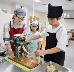 講師の浦木さん（左）と家庭用製麺機で中華麺作りに挑戦する児童ら