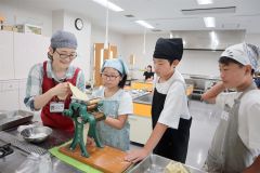 講師の浦木さん（左）と家庭用製麺機で中華麺作りに挑戦する児童ら