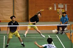 【男子個人戦ダブルス２回戦】第１ゲーム、後衛から打ち返す札幌龍谷の佐藤杏介（黑色ユニホーム、右）＝金野和彦撮影
