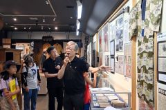 戦闘機などが描かれた着物の説明をする山本さんの話しに耳を傾ける参加者