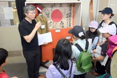 戦場での無事と、命運が長く続くことを願い兵士に贈られた日の丸の寄せ書きを説明する山本さんの話しに耳を傾ける子どもたち