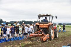 農機での収穫作業を見守る児童たち