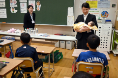 児童らに赤ん坊について教える帯広大谷短大看護学科の森田さん（左）と三田さん（右）